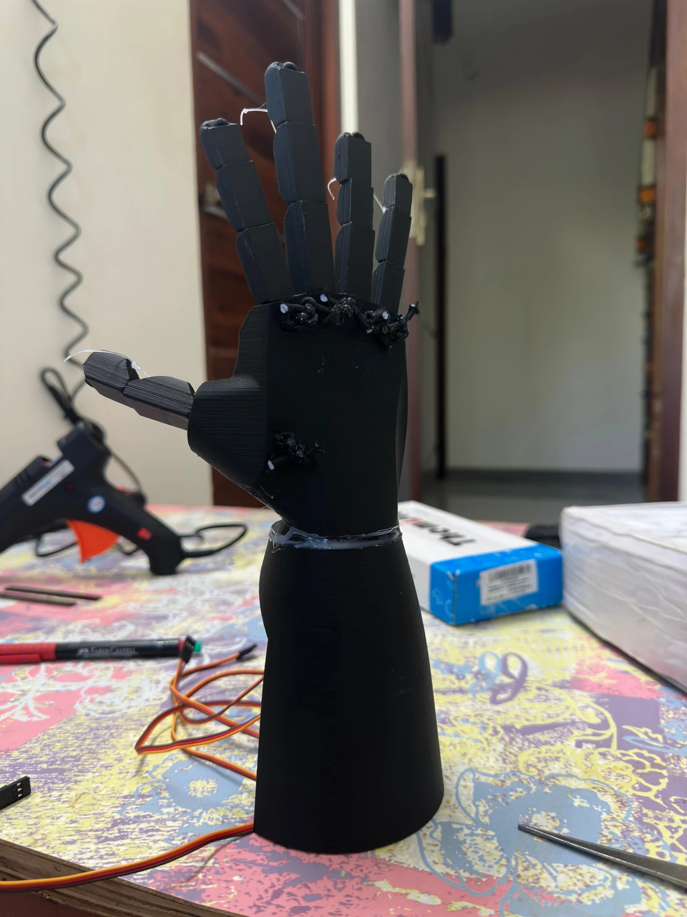 Assembled black robotic hand and forearm prototype standing on the workbench